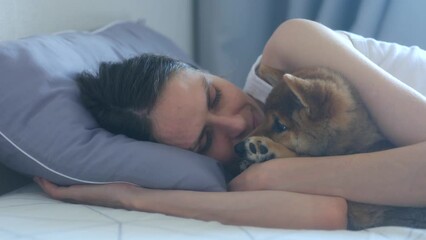 Happy young female owner hugs cute puppy shiba inu pet dog lying on bed together at home interior. Close up. domestic animals, concept of happiness, friendship and love between an animal and human