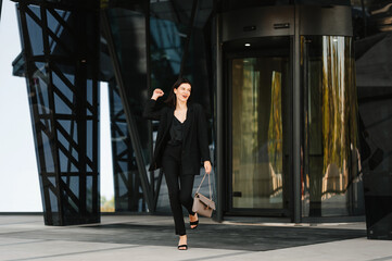 Young successful confident woman is walking off the work glass building.