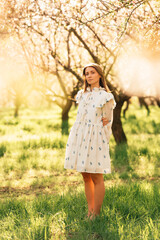 Young woman wearing white dress standing in almond orchard on a sunny day.