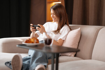 Young woman is having free time while sitting on couch and scrolling her phone.