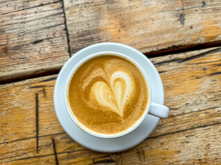 A cup of coffee latte on a wooden table. A mug of flat white coffee on a wooden background. Coffee art. Heart flower shape latte art.