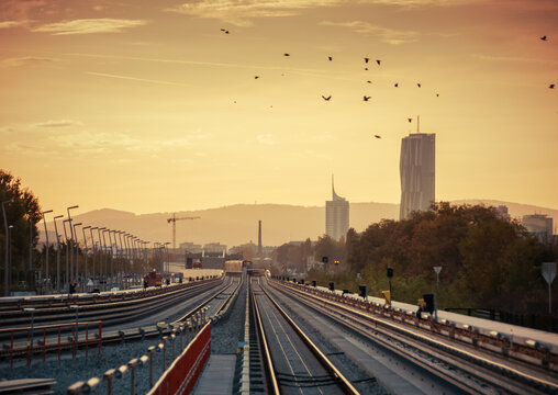 Elevated subway line in direction of Donaucity - diminishing perspective view. Sunset in the city, mountains in horizon. Flock of birds flying over the rails. Vienna, Austria - October 21, 2013.