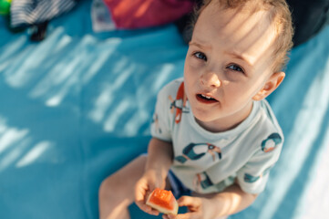 Headshot of a little boy eating watermelon on a beach.