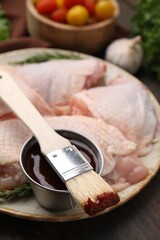 Plate with fresh marinade, raw chicken and basting brush on wooden table, closeup