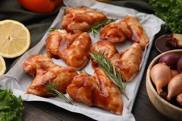 Raw marinated chicken wings, rosemary and other products on wooden table, closeup