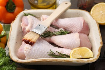Basting brush with marinade, raw chicken drumsticks, rosemary and lemon on table, closeup