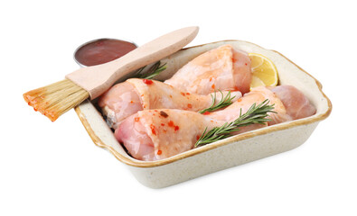 Fresh marinade, basting brush, raw chicken drumsticks, rosemary and lemon isolated on white