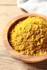 Dry curry powder in bowl on wooden table, closeup