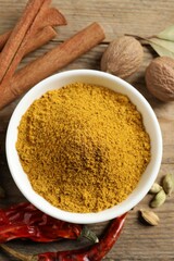 Dry curry powder in bowl and other spices on wooden table, flat lay