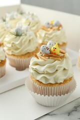 Tasty Easter cupcakes with vanilla cream on white marble table, closeup