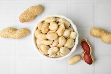 Fresh peeled peanuts in bowl on white tiled table, flat lay