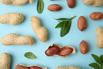 Fresh peanuts and leaves on light blue table, flat lay