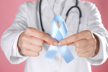 International Psoriasis Day. Doctor with light blue ribbon as symbol of support on pink background,...