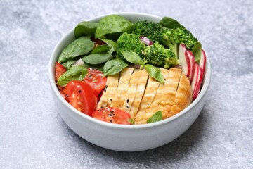 Healthy meal. Delicious chicken, vegetables and spinach in bowl on light grey table, closeup