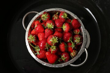 Metal colander with fresh wet strawberries in sink, top view