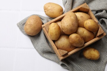Raw fresh potatoes and wooden crate on white tiled table, top view