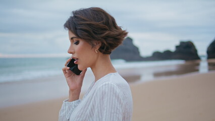 Gorgeous brunette talking mobile phone closeup. Beautiful girl walking beach