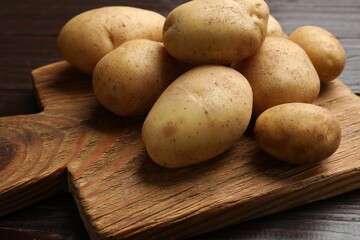 Raw fresh potatoes and cutting board on wooden table