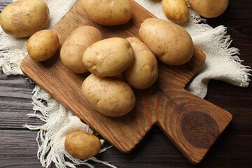 Raw fresh potatoes and cutting board on wooden table, top view