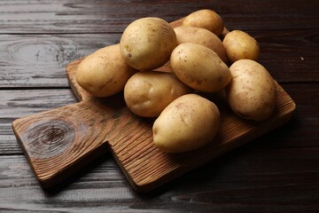 Raw fresh potatoes and cutting board on wooden table