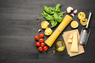 Different types of pasta, products, peppercorns and garter on dark wooden table, flat lay. Space...