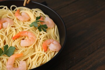 Tasty spaghetti with shrimps and parsley in bowl on wooden table, closeup. Space for text