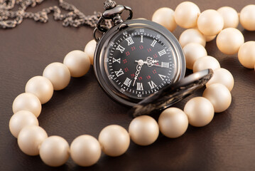 Antique pocket watch and pearl necklace on leather surface, selective focus