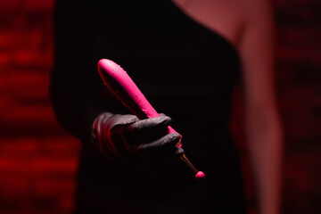 Burgundy stylish dildo for masturbation in the hand of a girl wearing black gloves on a red background. Nozzle for clitoral stimulation. Sex shop Adult store