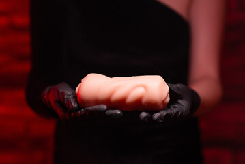 Sex toys for men. An artificial vagina made of silicone for masturbation in the hands of a girl in black gloves and a black dress on a red background. Sex shop Adult store