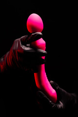 Pink stylish vibrator for masturbation in the hands of a girl in black gloves on a black background. Massager with multiple speeds. Products for sex shop, gifts for adults