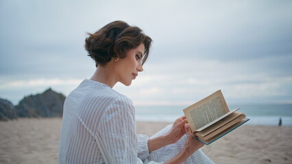 Thoughtful woman holding book at sea beach closeup. Focused model flipping pages