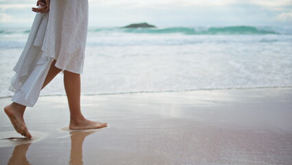 Legs going summer beach on cloudy day closeup. Relaxed woman leaving footprints