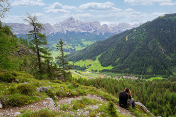 Fototapeta premium Young man photographer taking pictures of the Dolomite mountains Italy. person sitting on the grass, hiking mountains