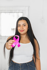 young latin brunette woman holding in her hand a pink ribbon symbol of the fight against breast cancer