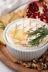 Board with tasty baked camembert and rosemary in bowl on table, closeup