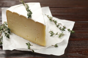 Piece of tasty camembert cheese and thyme on wooden table, closeup