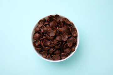 Breakfast cereal. Chocolate corn flakes in bowl on light blue table, top view