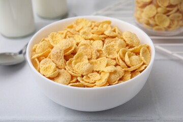 Tasty crispy corn flakes in bowl on white table, closeup. Breakfast cereal
