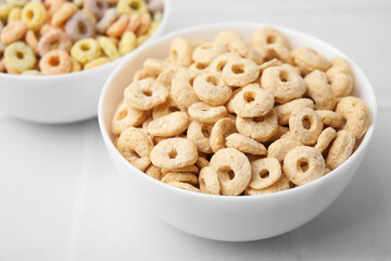 Tasty cereal rings in bowls on white table, closeup
