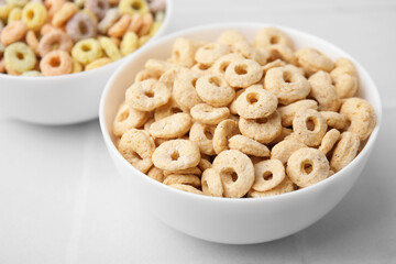 Tasty cereal rings in bowls on white table, closeup