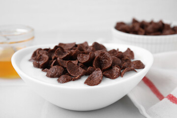 Breakfast cereal. Chocolate corn flakes and milk in bowl on white table, closeup