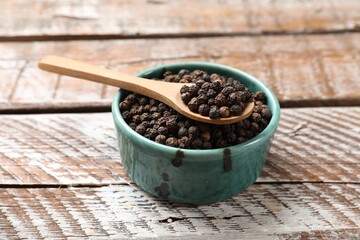 Aromatic spice. Black pepper in bowl and spoon on wooden table