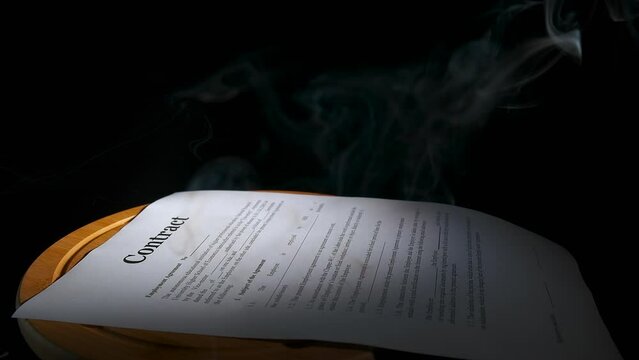 Burns paper contract on black background. A view of paper in fume on the table on the black background.