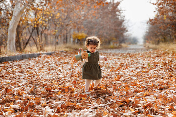 Child s autumn tale. Adorable little girl walking among golden autumn leaves with her teddy