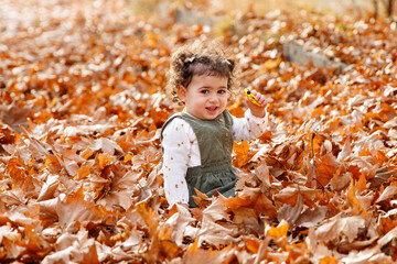 Childhood and fall. A child sits among a myriad of fallen leaves and holding her car toy