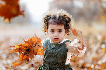 Close up of astonished child holding crisp leaves, standing in a world of fallen foliage