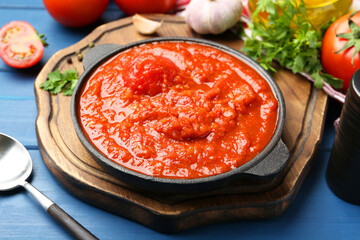 Homemade tomato sauce in bowl, spoon and ingredients on blue wooden table