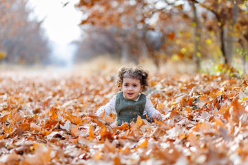 Curly hair child playing among the rustling autumn leaves