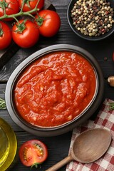 Homemade tomato sauce in bowl, spoon and fresh ingredients on black wooden table, flat lay
