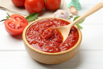 Homemade tomato sauce and spoon in bowl on white wooden table, closeup